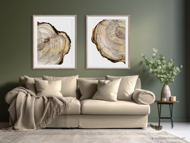 K&ouml;nnte beinhalten: Zwei gerahmte Drucke von Aquarellmalereien von Baumringen. Die Drucke h&auml;ngen an einer Salbeigr&uuml;nen Wand &uuml;ber einem beigen Sofa mit Kissen und einer Decke.