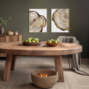 K&ouml;nnte beinhalten: Ein runder Esstisch aus Holz mit nat&uuml;rlicher Holzmaserung. Der Tisch ist mit einer Sch&uuml;ssel gr&uuml;ner &Auml;pfel und einem geflochtenen Korb mit Orangen gedeckt. Zwei gerahmte Drucke von Baumringen h&auml;ngen an der Wand hinter dem Tisch.
