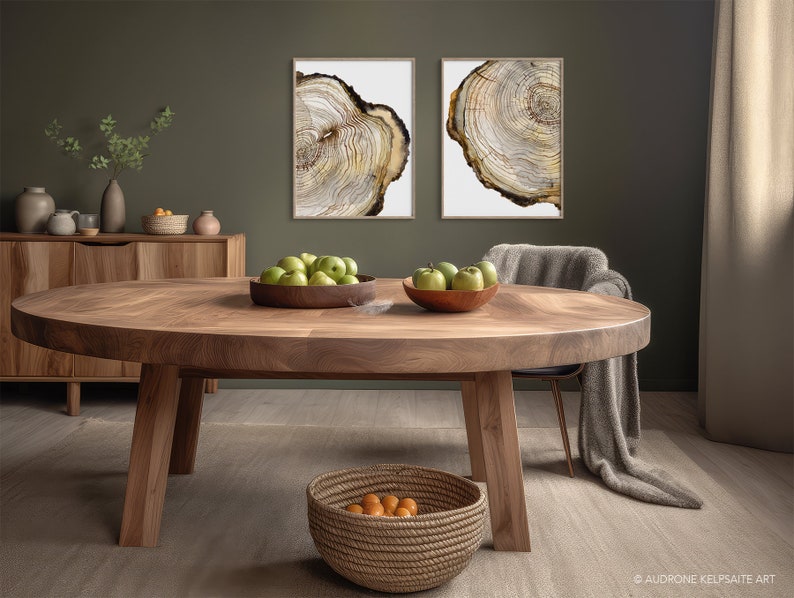 K&ouml;nnte beinhalten: Ein runder Esstisch aus Holz mit nat&uuml;rlicher Holzmaserung. Der Tisch ist mit einer Sch&uuml;ssel gr&uuml;ner &Auml;pfel und einem geflochtenen Korb mit Orangen gedeckt. Zwei gerahmte Drucke von Baumringen h&auml;ngen an der Wand hinter dem Tisch.