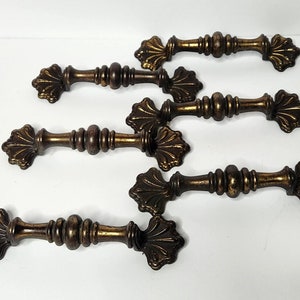 May include: Five antique brass cabinet knobs with ornate floral designs. Each knob has a decorative, fluted, cylindrical stem.