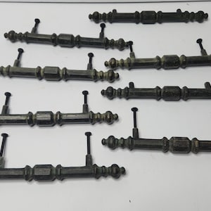 May include: Eight antique-style cabinet pulls with a dark bronze finish. Each pull has a decorative design and a black screw.
