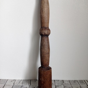 May include: A dark brown wooden mallet with a rounded head and a long, slender handle. The handle has a decorative, slightly bulbous section in the middle.