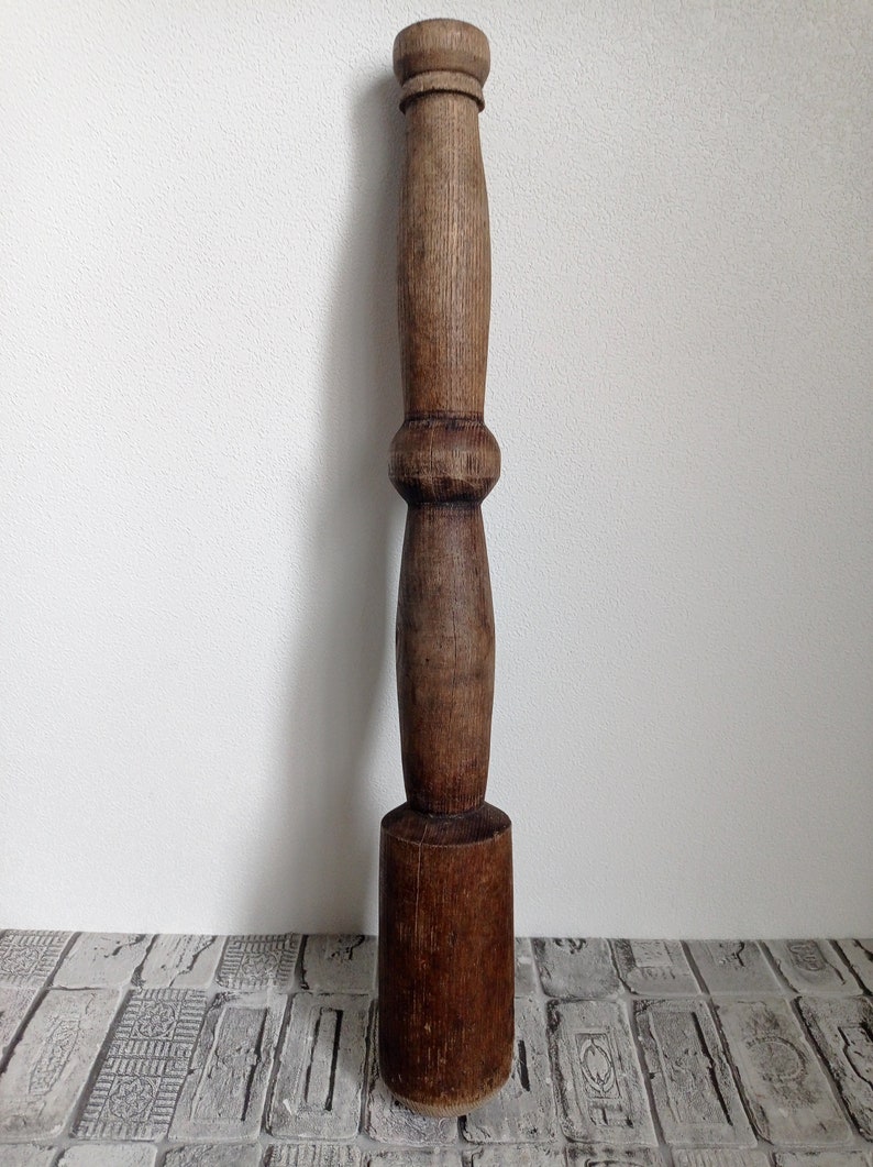 May include: A dark brown wooden mallet with a rounded head and a long, slender handle. The handle has a decorative, slightly bulbous section in the middle.
