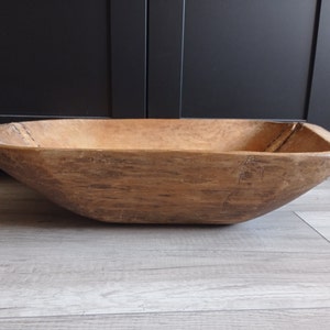 May include: A large, wooden, oval-shaped dough bowl with a natural wood finish. The bowl has a rustic, vintage look and is perfect for serving or displaying.