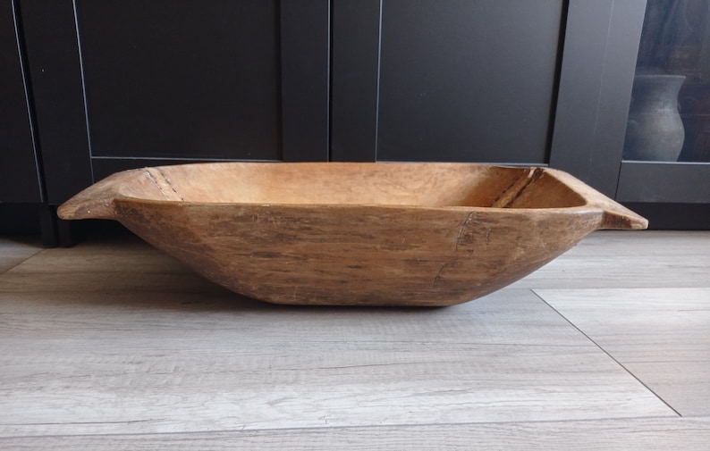 May include: A large, wooden, oval-shaped dough bowl with a natural wood finish. The bowl has a rustic, vintage look and is perfect for serving or displaying.