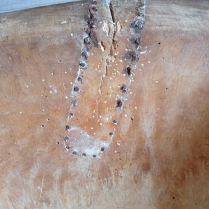 May include: Close-up of a wooden bowl with a crack down the center. The crack is reinforced with a leather patch and metal tacks.