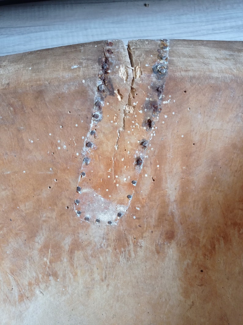 May include: Close-up of a wooden bowl with a crack down the center. The crack is reinforced with a leather patch and metal tacks.