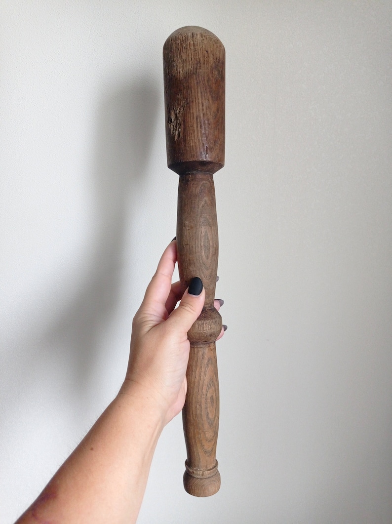 May include: A wooden pestle with a rounded head and a long, cylindrical handle. The handle has a slight curve in the middle.