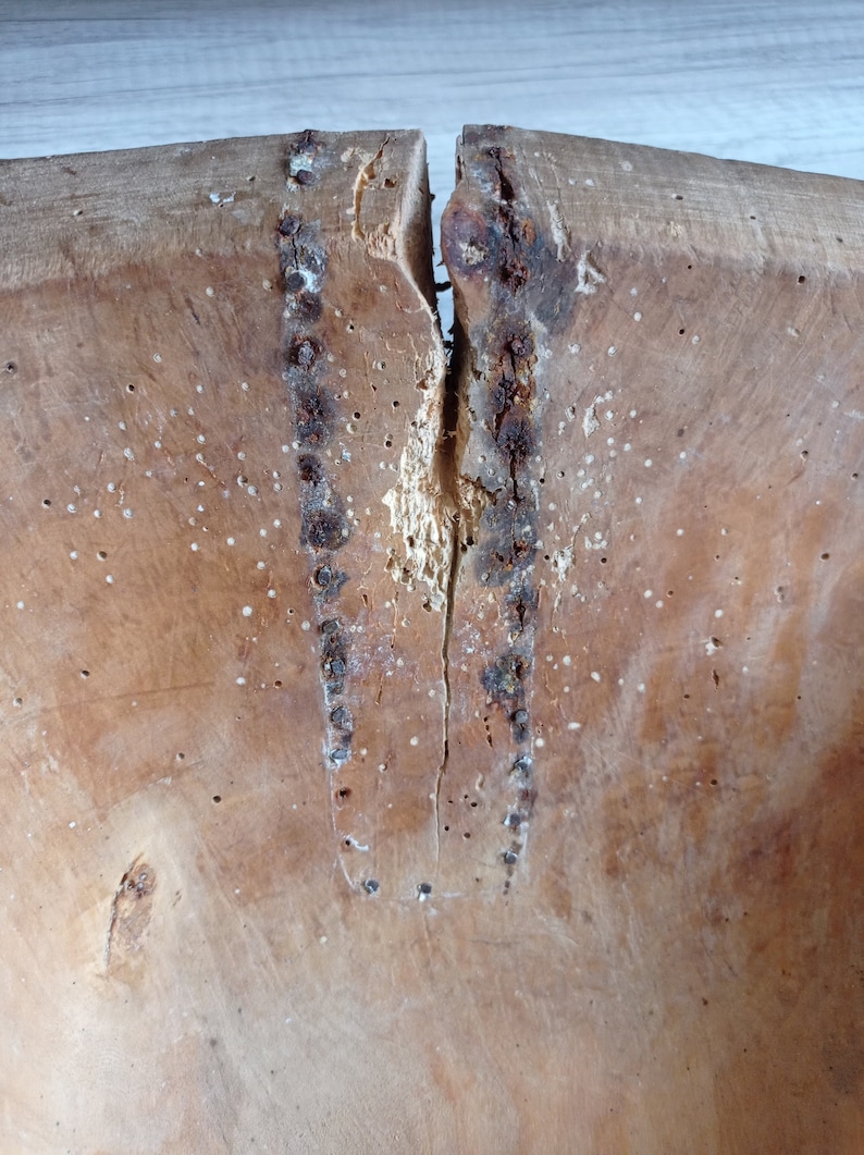 May include: A close-up of a wooden bowl with a crack down the center. The bowl is made of light brown wood and has a rough texture. There are several small holes in the wood, likely from insects.