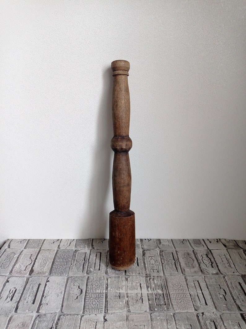 May include: A wooden pestle with a rounded head and a long, slender handle. The pestle is brown and has a smooth, polished finish.