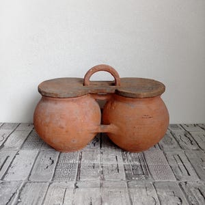 May include: A set of two terracotta pots with wooden lids and a wooden handle. The pots are connected by a wooden bridge.