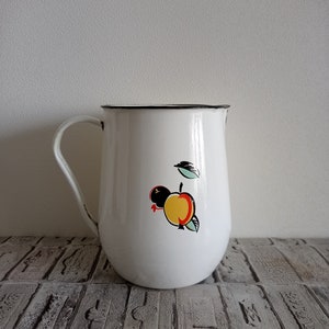 Könnte beinhalten: Weißer Emaille-Krug mit schwarzem Rand und handgemaltem Design eines gelben und roten Apfels mit einem grünen Blatt.