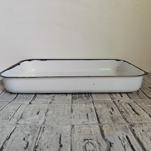 May include: White enamel baking dish with a black rim. The dish is rectangular and has a slightly rounded bottom.