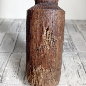 May include: A close-up of a wooden rolling pin with a worn, rustic finish. The pin has a round shape and is made of dark brown wood with visible grain patterns. There are signs of wear and tear on the surface, including a small knot and a few scratches.