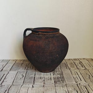 May include: A dark brown clay pot with a handle. The pot has a rough, textured surface and appears to be old.