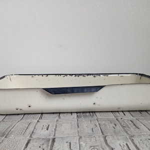 Op de afbeelding: Crèmekleurige rechthoekige emaille bak met een donkerblauwe rand en handvat. De bak vertoont tekenen van slijtage, met afgebladderde verf en wat roestvlekken. De bak is waarschijnlijk vintage en geschikt voor keuken of woondecoratie.