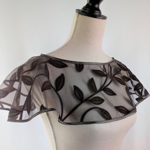 Puede incluir: Un collar de encaje transparente marrón con un diseño de hojas. El collar está en un maniquí blanco.