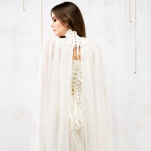 May include: A white sheer cape with a white lace-up corset. The cape is flowing and the corset is cinched at the waist.