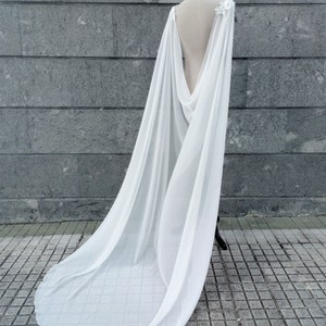 Pu&ograve; includere: Una cappa bianca in chiffon con scollo drappeggiato e una lunga coda. La cappa &egrave; drappeggiata su un manichino ed &egrave; realizzata in un tessuto leggero.