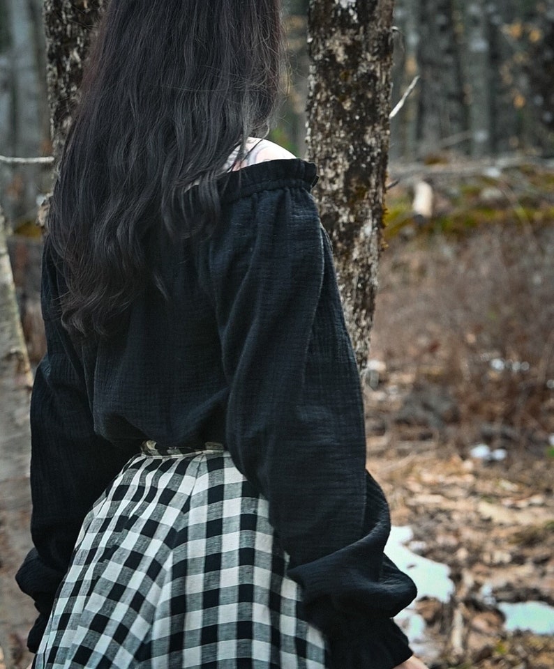 May include: A woman wearing a black off-the-shoulder blouse with long sleeves and a black and white checkered skirt.