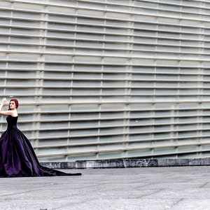 May include: A floor-length, strapless black ball gown with a fitted bodice and a voluminous, full skirt that extends into a long train. The garment features a smooth, solid-colored fabric and a structured silhouette that flares from the waist down.