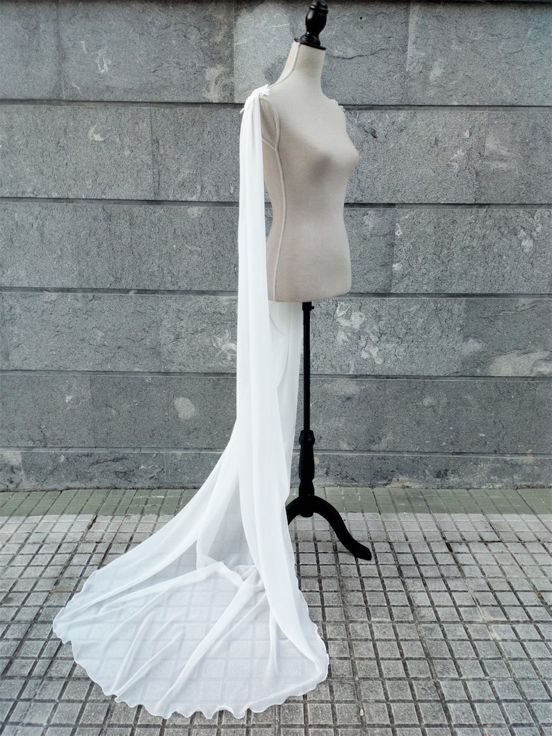 Pu&ograve; includere: Un'ampia cappa da sposa bianca e trasparente con una lunga coda, drappeggiata su un manichino. La cappa &egrave; realizzata in un tessuto leggero e ha un design delicato e fluido.