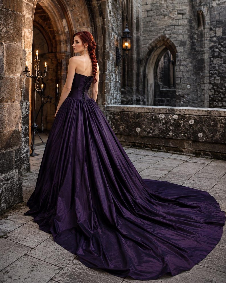 May include: A floor-length, strapless deep purple gown featuring a fitted bodice with a lace-up back closure and a voluminous, pleated skirt that extends into a long train. The fabric has a subtle sheen and a structured, full silhouette.