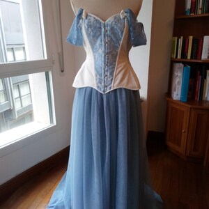 May include: A white and blue lace corset with a blue tulle skirt. The corset has a sweetheart neckline and is strapless. The skirt is full and flowing.