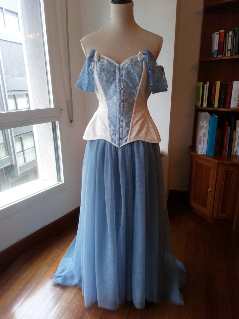 May include: A white and blue lace corset with a blue tulle skirt. The corset has a sweetheart neckline and is strapless. The skirt is full and flowing.