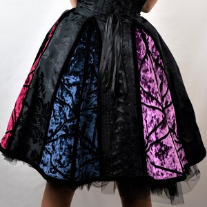 May include: A black, velvet, and satin dress with a fitted bodice and a full skirt. The skirt is made of four panels of different colors: red, blue, black, and purple. The dress has a lace-up back.