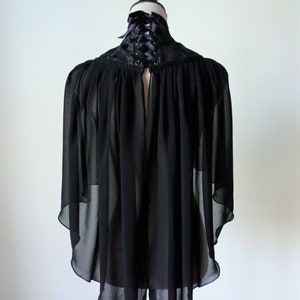 May include: Black sheer cape with a lace collar and a black ribbon tie at the back of the neck.