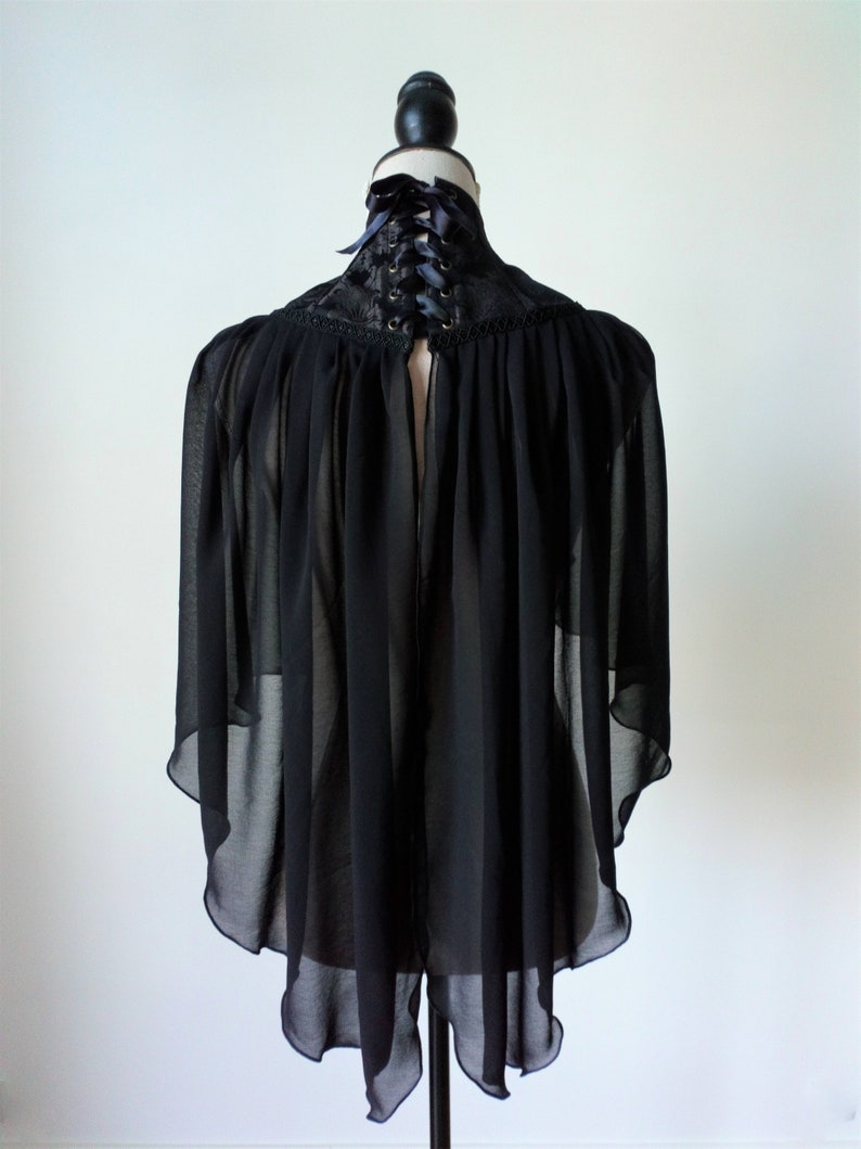 May include: Black sheer cape with a lace collar and a black ribbon tie at the back of the neck.