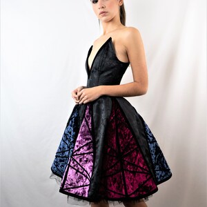 May include: A black strapless dress with a deep V-neckline and a geometric pattern on the skirt. The skirt is made of a velvet fabric and has a tulle underskirt. The dress is fitted at the bodice and flows out at the skirt.