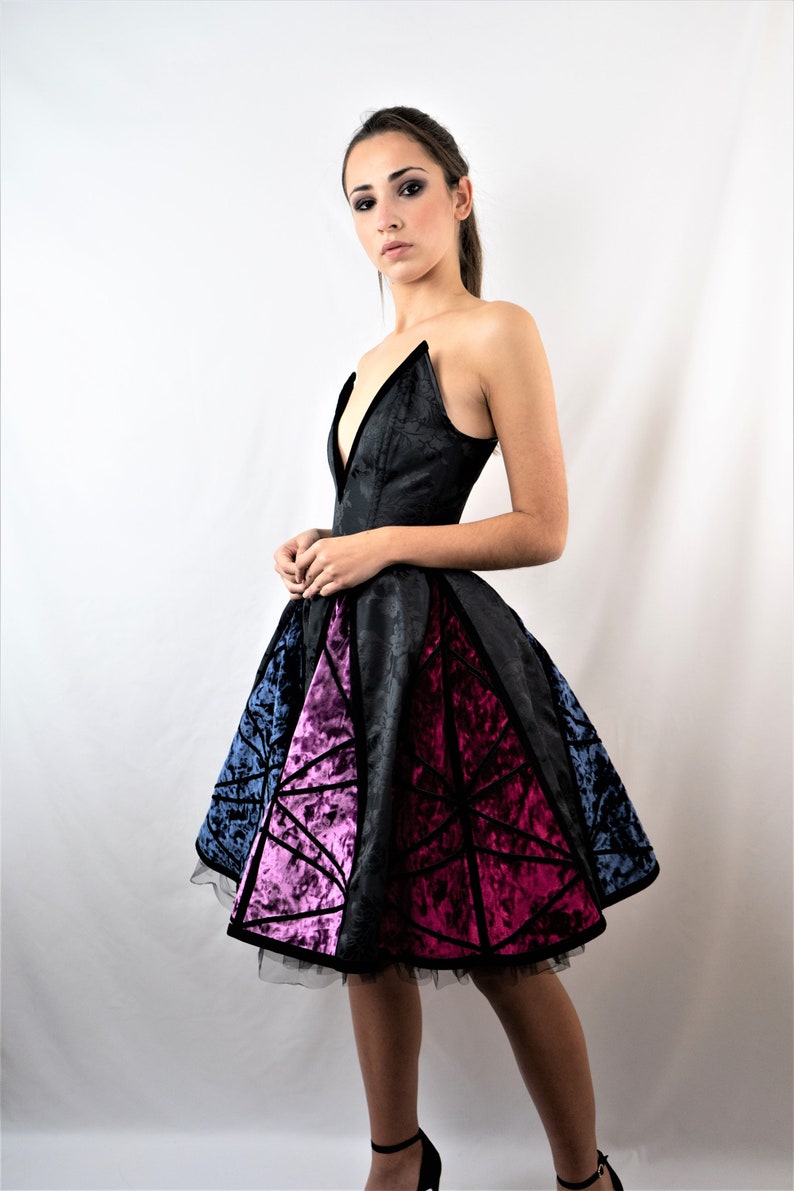 May include: A black strapless dress with a deep V-neckline and a geometric pattern on the skirt. The skirt is made of a velvet fabric and has a tulle underskirt. The dress is fitted at the bodice and flows out at the skirt.