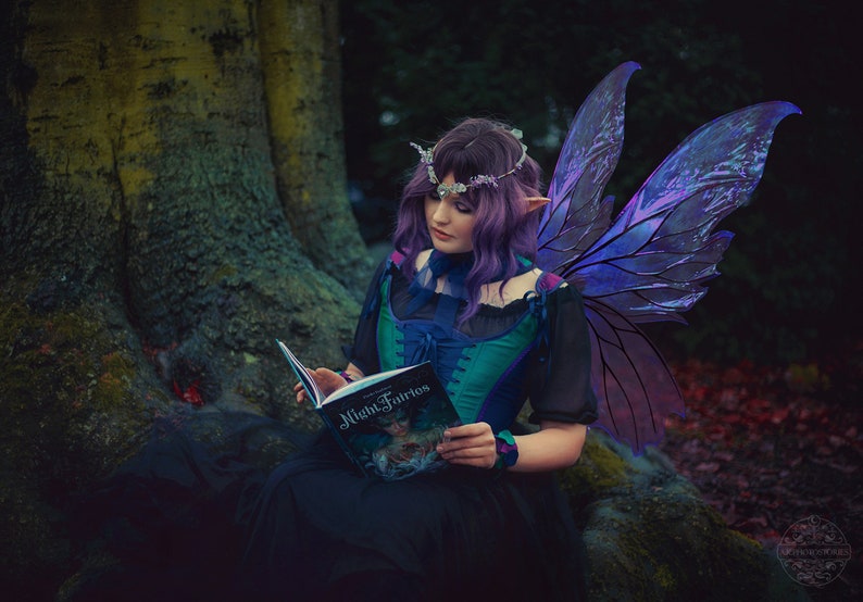 May include: A woman with purple hair and iridescent fairy wings sits reading a book titled "Night Fairies".
