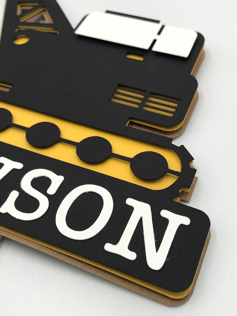 May include: Black and yellow construction vehicle cutout with the name "NASON" in white letters.