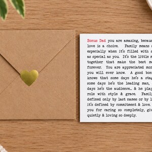 May include: A square white greeting card with black typewriter-style text beginning with Bonus Dad in red, expressing appreciation for a bonus father. Beside it sits a square brown kraft paper envelope sealed with a small gold heart sticker.