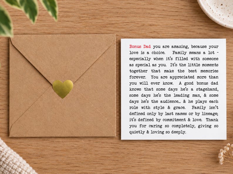 May include: A square white greeting card with black typewriter-style text beginning with Bonus Dad in red, expressing appreciation for a bonus father. Beside it sits a square brown kraft paper envelope sealed with a small gold heart sticker.