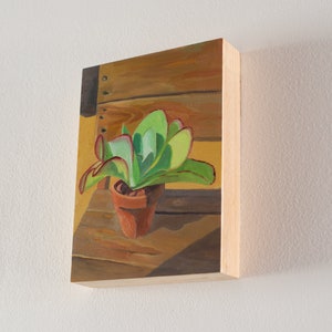 Puede incluir: Pintura de una planta suculenta en una maceta de terracota. La planta tiene hojas verdes con bordes rojos. La maceta est&aacute; sobre una superficie de madera, con un fondo amarillo c&aacute;lido. La obra de arte est&aacute; sobre un panel de madera.
