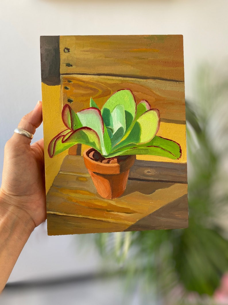 Puede incluir: Pintura al &oacute;leo de una planta suculenta en una maceta de terracota. La planta tiene hojas verdes con bordes rojos. La pintura est&aacute; ambientada sobre un fondo de madera con sombras.
