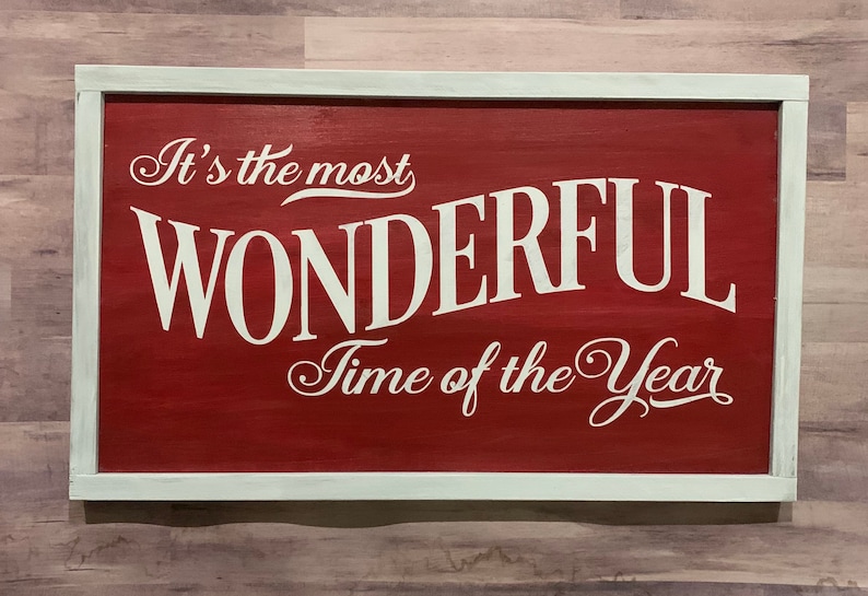 Puede incluir: Un letrero de madera rojo con marco blanco y el texto "It's the most WONDERFUL Time of the Year" en letras blancas cursivas.