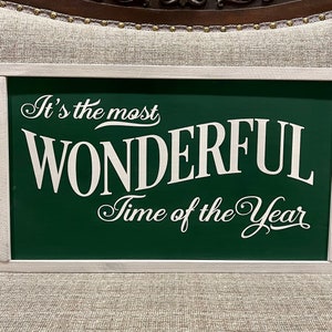 Puede incluir: Un letrero verde enmarcado en blanco con el texto "It's the most WONDERFUL Time of the Year" en fuente blanca cursiva.