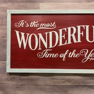 Puede incluir: Un letrero de madera rojo con letras blancas que dice "It's the most WONDERFUL Time of the Year". El letrero tiene un marco blanco.