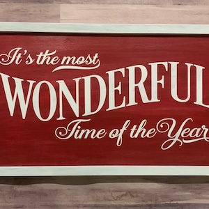 Puede incluir: Un letrero de madera rojo con letras blancas que dice "It's the most wonderful time of the year". El letrero est&aacute; enmarcado con un borde blanco.