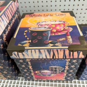 May include: A square decorative storage box featuring a lid with a coffee mug graphic and the text Whole Latte Love. The box has dark quilted sides with gold-tone metal corner protectors and a zebra print border around the lid edge.