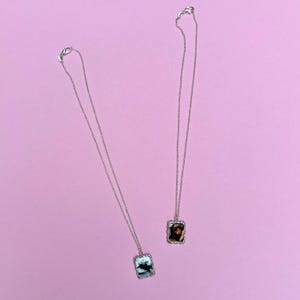 Peut inclure: Deux colliers en argent avec des pendentifs rectangulaires repr&eacute;sentant des photos en noir et blanc. Les pendentifs ont une bordure d&eacute;corative.