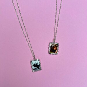 Peut inclure: Deux colliers en argent avec des pendentifs rectangulaires repr&eacute;sentant des photos en noir et blanc. Les pendentifs ont une bordure d&eacute;corative et orn&eacute;e.