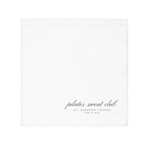 May include: A square white paper napkin featuring black text in the bottom right corner. The text reads "pilates sweat club" in a cursive script font, followed by the words "EST. WHENEVER I BOOKED THE CLASS" in a simple sans-serif typeface.