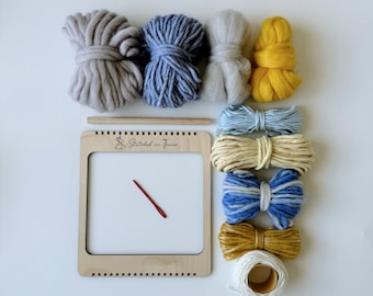 May include: A wooden loom with a needle and yarn in various colors, including gray, blue, yellow, and white. The loom has the text "Stitched in June" printed on it.