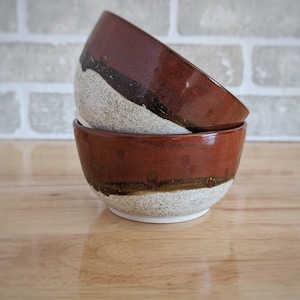 May include: Three ceramic bowls stacked on top of each other. The bowls are brown with a white glaze and a black stripe around the rim.
